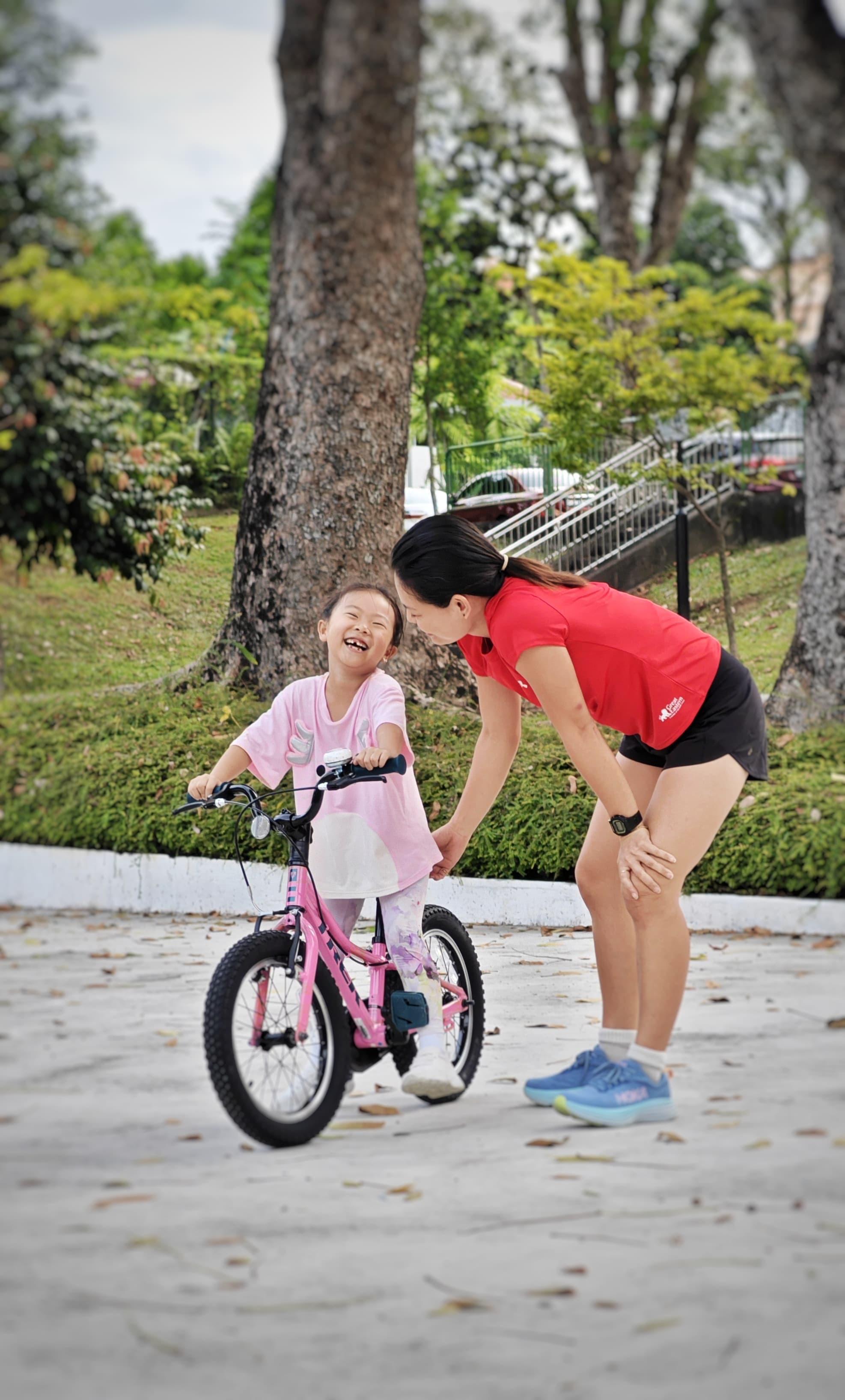 A child laughs on a pink bicycle after pedalling solo for the first time at a OhmRide lesson